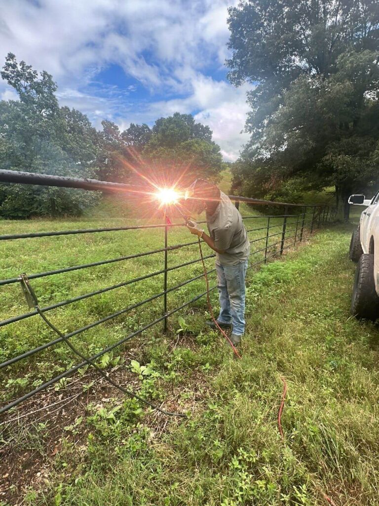 Bright welding spark as a fence installer works on a black welded pipe fence in Northwest Arkansas
